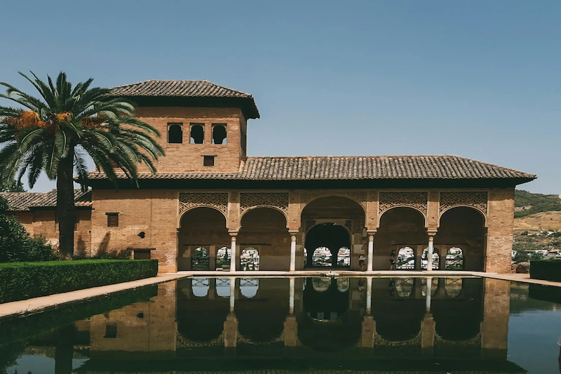 Moorish-inspired house at the Alhambra in Granada with a reflecting pool and a palm tree.