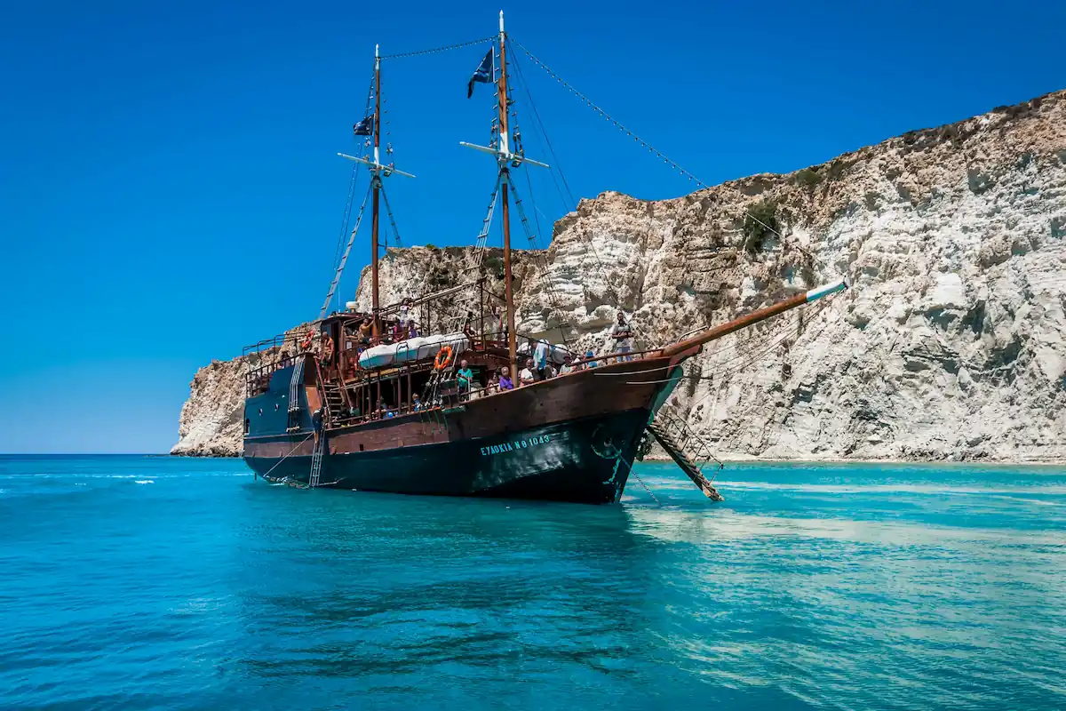 Historic boat sailing in turquoise waters near cliffs in Crete.