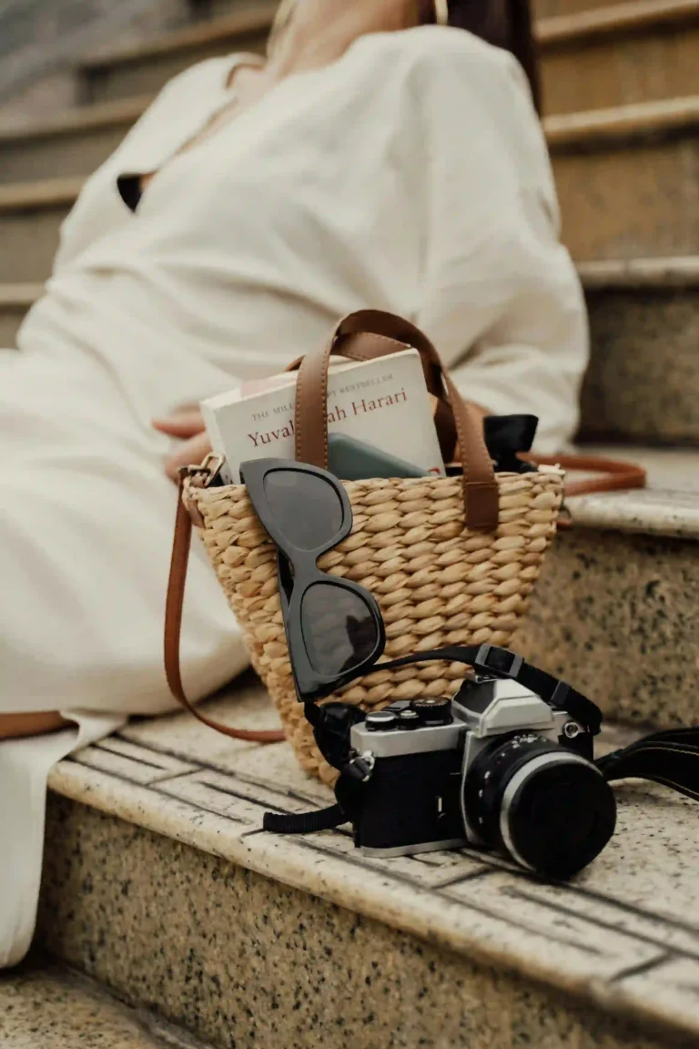 A wicker bag containing a book by Yuval Noah Harari, accompanied by sunglasses and a camera.