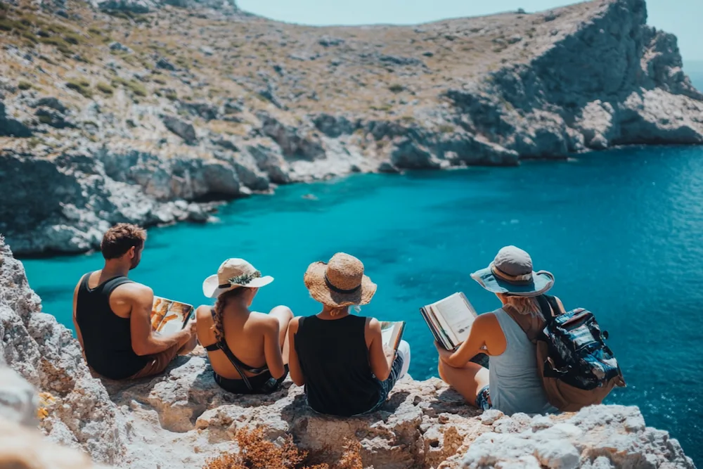 Group of literary travelers reading by the sea in Crete, sharing a moment of exchange.