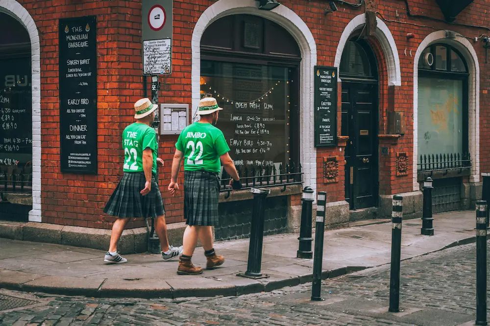 Two Irish people in traditional attire walking down a lively street in Dublin.